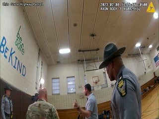 This photo provided by Ohio State Highway Patrol shows police bodycam footage of NewsNation correspondent Evan Lambert interaction with the leader of the Ohio National Guard Wednesday, Feb. 8, 2023 in the gymnasium of an elementary school in East Palestine, Ohio. Lambert was charged with criminal trespass and resisting arrest after authorities said he was told to stop his live broadcast and then refused their orders to leave the news conference with Ohio Gov. Mike DeWine. (Ohio State Highway Patrol via AP)