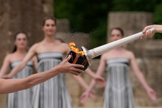 Actress Mary Mina, playing high priestess, right, lights a torch during the official ceremony of the flame lighting for the Paris Olympics, at the Ancient Olympia site, Greece, Tuesday, April 16, 2024. The flame will be carried through Greece for 11 days before being handed over to Paris organizers on April 26. (AP Photo/Thanassis Stavrakis)