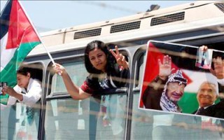 Una de las prisioneras palestinas liberadas por las autoridades israelíes saluda a sus familiares mientras el autobús en el que viaja pasa el puesto de control de Bitunia con destino a la ciudad Cisjordana de Ramala hoy viernes 20 de julio. (EFE)