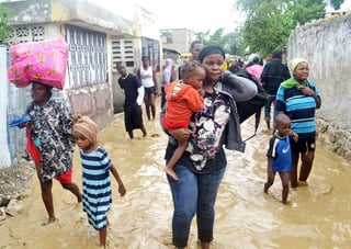 En Haití.  Una mujer carga a su hija mientras camina en una calle inundada en Puerto Príncipe, Haití.