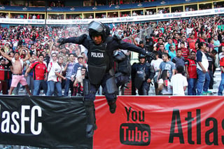 Un Policía de Guadalajara salta mientras los aficionados le arrojan líquidos a sus espaldas. (Jam Media)