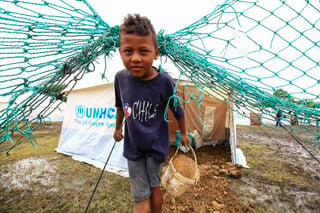 Escenario. Un niño en un campo de refugiados sostiene una cubeta para ir por agua. 