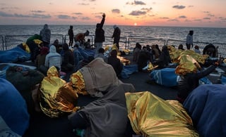 Un grupo de personas rescatadas en la cubierta de un buque naval italiano ve como el sol se pone en el Mediterráneo. (ONU)