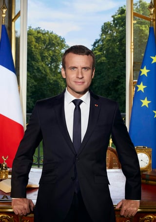 En la imagen, Macron aparece retratado entre las banderas de Francia y de Europa, en un despacho del palacio presidencial del Elíseo en el que se perciben sus jardines al fondo. (AP)