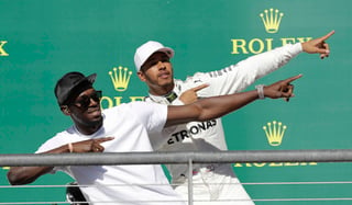 Lewis Hamilton y Usain Bolt hacen la pose clásica del jamaiquino, en la premiación del GP de EU. (AP)