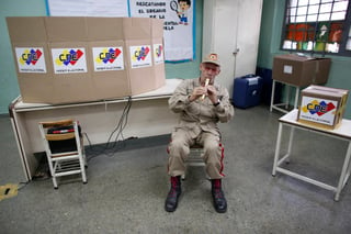 Pocos. Un miembro de la milicia bolivariana toca la flauta en una mesa de votación durante las elecciones presidenciales en Caracas. (AP)