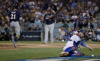 El cubano Yasmani Grandal, cátcher de los Dodgers, persigue un wild pitch, mientras Travis Shaw, de los Brewers, anota.