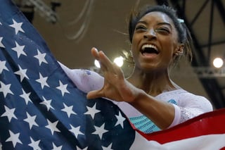 La medallista de oro y cuatro veces campeona mundial de prueba combinada Simone Biles celebra con la bandera de su país.