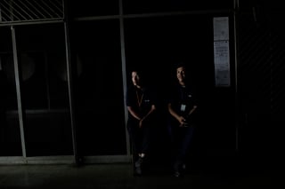 Personas que usan uniformes del periódico El Universal se sientan en la oscura oficina de un edificio de oficinas durante un apagón en Caracas, Venezuela. (AP)