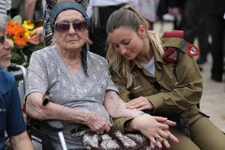 La soldado israelí Shira Tessler sostiene la mano de su abuela Hanna Tessler, superviviente del Holocausto, mientras observa el tatuaje de su brazo durante una ceremonia por el Día de Recuerdo del Holocausto en el complejo conmemorativo Yad Vashe. (EFE)