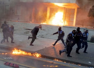 Oficiales de policía huyen luego de que una bomba improvisada fue lanzada cerca de ellos fuera de un edificio de Gobierno. (EFE)