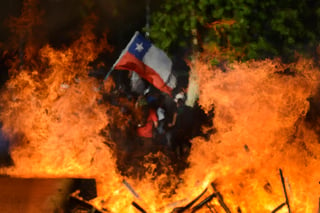 Visto a través de una barricada callejera en llamas, un manifestante antigubernamental ondea una bandera chilena el 28 de octubre.(AP)