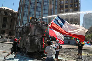 Manifestantes antigubernamentales se enfrentan a un cañón de agua de la policía cerca del palacio presidencial de La Moneda, en Chile. (AP)