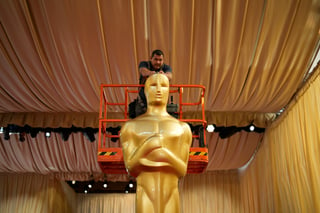 Un trabajador ayuda a colocar una estatua de los Oscar en la alfombra roja previo a la 96a entrega de los Premios de la Academia. (AP)