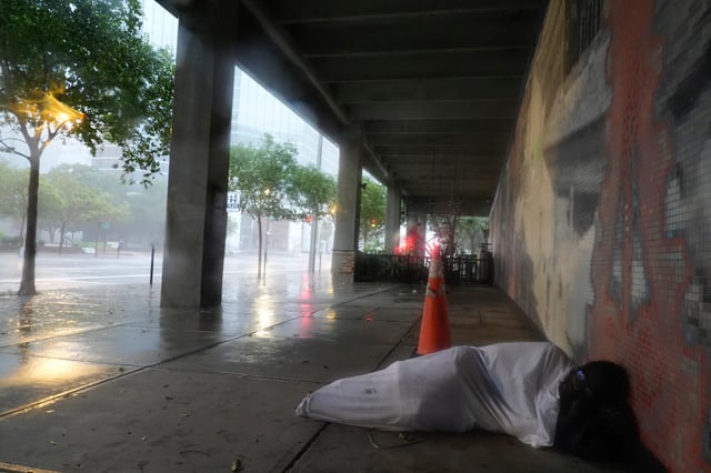 Melvin Lee Hicks, un indigente, se cubre con una sábana cerca de un hotel cercano en un estacionamiento del centro de Tampa, Florida, ante la aproximación del huracán Milton, el miércoles 9 de octubre de 2024. (AP Foto/Rebecca Blackwell)