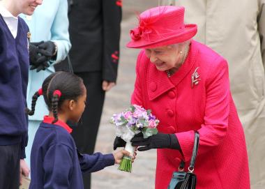 Niños de escuelas locales, que portaban banderas inglesas, fueron los primeros en saludar a la Reina, que llevaba un abrigo rojo y una pamela a tono, que acompañó con un collar de perlas