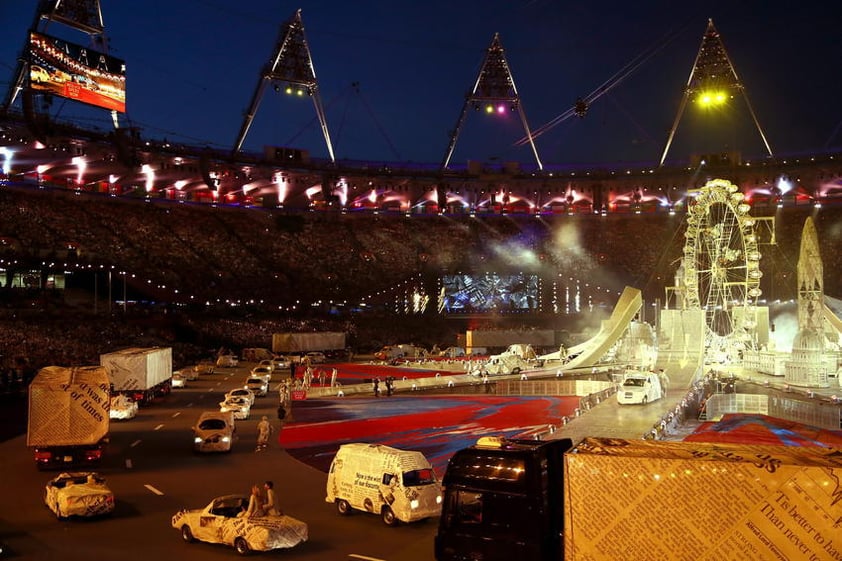 Taxis londinenses cubiertos con papel de periódico recorren las pistas del hasta ayer estadio de atletismo, sobre un escenario con los colores difuminados de la bandera británica diseñado por el artista británico Damien Hirst.