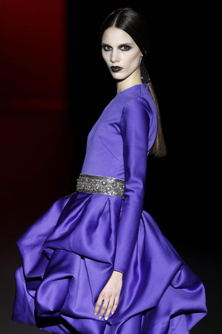 Una modelo luce un vestido de Hannibal Laguna, con un vestido de manga larga de color morado, el cual destaca por un cinto plateado que combina con los colores de la temporada para vestidos de noche.