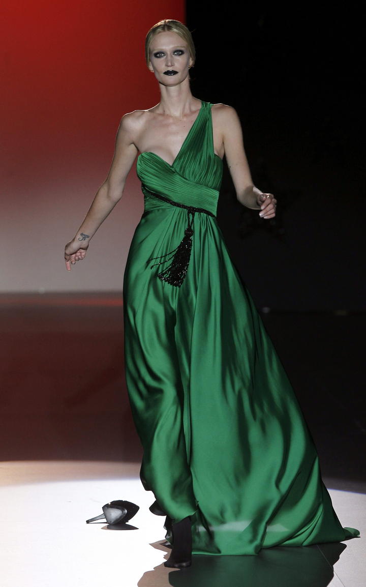 Una modelo, tras caerle un zapato, en el desfile de Hannibal Laguna, luce un hermoso vestido en un verde vivo, usando un halter para resaltar un un cinto negro.