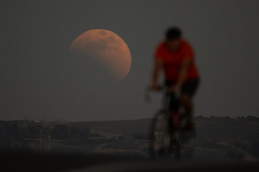 A lunar eclipse is seen behind a cyclist during the first blood moon of the year, in Irwindale, Calif. May 15, 2022. (AP Photo/Ringo H.W. Chiu)