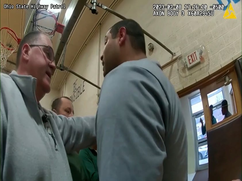 This photo provided by Ohio State Highway Patrol shows police bodycam footage of NewsNation correspondent Evan Lambert interaction with authorities Wednesday, Feb. 8, 2023 in the gymnasium of an elementary school in East Palestine, Ohio. Lambert was charged with criminal trespass and resisting arrest after authorities said he was told to stop his live broadcast and then refused their orders to leave the news conference with Ohio Gov. Mike DeWine. (Ohio State Highway Patrol via AP)