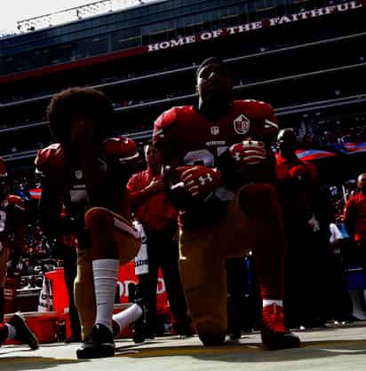 El mariscal de campo Colin Kaepernick (i) y el safety Eric Reid (d) se hincan durante el himno nacional de los Estados Unidos en un partido de 2016. (AGENCIA) 