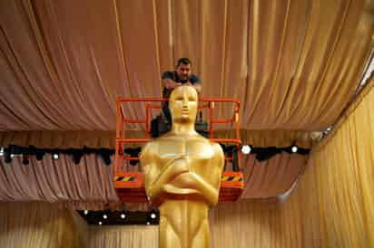 Un trabajador ayuda a colocar una estatua de los Oscar en la alfombra roja previo a la 96a entrega de los Premios de la Academia. (AP)