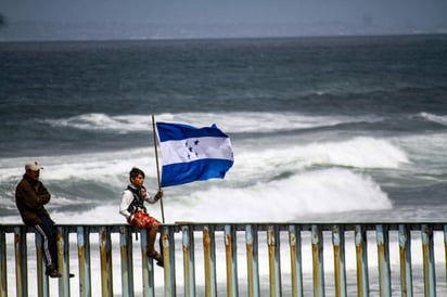 Los migrantes de la caravana que cruzó el territorio mexicano cantaron ayer sus himnos nacionales y ondearon sus banderas sobre el muro fronterizo de Estados Unidos. (EFE)