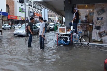 Un vendedor de gorditas de cocedor sube a su triciclo para evitar ser alcanzado por el nivel del agua, mientras otros peatones intentan cruzar la calle, justo en la esquina de Acuña y Juárez, en el Centro de Torreón.
