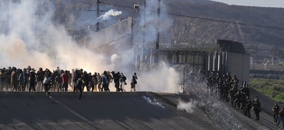 Confrontación. Un grupo de migrantes de la caravana de centroamericanos que avanzó ayer hacia la garita de San Ysidro (EE.UU.) se desvió de la ruta prevista para intentar cruzar el muro fronterizo por otros puntos, en tanto la policía fronteriza estadounidense les lanzó gas lacrimógeno. (EFE)