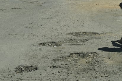 Hay baches y pavimento dañado en el sitio.