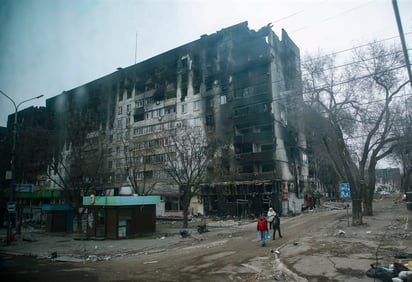 Una foto tomada durante una visita a Mariúpol organizada por el ejército ruso muestra a la población local llevando agua cerca de un edificio de apartamentos devastados y quemados en el centro de Mariípol.
