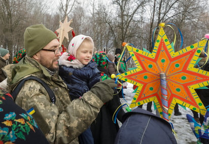 Una niña juega con una 'Estrella de Belén' mientras es sostenida en brazos de su padre, miembro de las Fuerzas de Defensa Territorial de Ucrania, durante una celebración navideña en el pueblo de Pyrogovo, cerca de Kiev, Ucrania. (SERGEY DOLZHENKO / EFE)