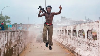 El combatiente Joseph Duo celebra tras haber lanzado una granada a los rebeldes desde un puente, en Liberia (2003), por Chris Hondros. 