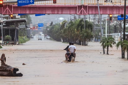 Dos personas en una moto transitan por una calle inundada este jueves en Acapulco. (AGENCIAS)