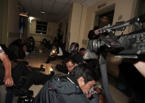 Miembros de la prensa nacional e internacional se protegen en el piso del fuego cruzado mientras militares sacan al presidente de Ecuador.