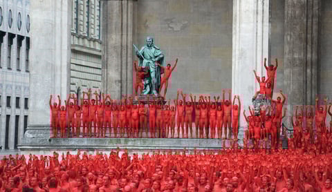 Poco antes del amanecer y a una temperatura de apenas 13 grados, Tunick empezó a disparar su objetivo para tomar las primeras instantáneas en la famosa avenida muniquense de Ludwigstrasse, donde cientos de cuerpos pintados de rojo escenificaron una llama en alusión al emblemático inframundo de Wagner "el hogar del nibelungo".