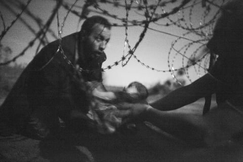 La “World Press Photo del Año” es una fotografía del australiano Warren Richardson, en blanco y negro, en la que se observa cuando un hombre, con los ojos fijos en el horizonte, pasa a un bebé debajo de una cerca de alambre de púas en la frontera entre Hungría y Serbia, bajo la luz de la Luna.