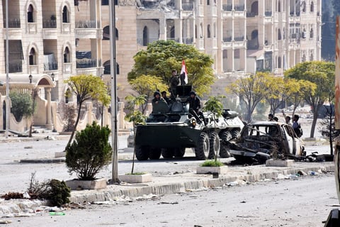Soldados sirios patrullan en su vehículo blindado junto a edificios dañados en las aldeas occidentales de Alepo del distrito de al-Assad.