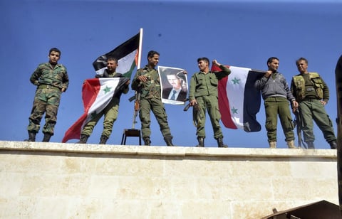 Miembros del Ejército Árabe Sirio (SAA) ondeando banderas nacionales y sujetando carteles con el rostro del presidente, Bachar al Asad, en ya tomada localidad de al-Hader, en Alepo.