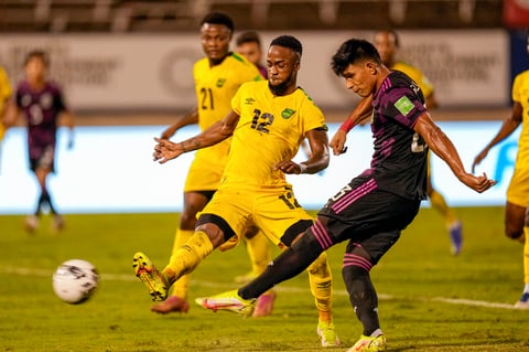Mexico’s Jesus Gallardo connects a shot challenged by Jamaica's Junior Flemmings during a qualifying soccer match for the FIFA World Cup Qatar 2022 in Kingston, Jamaica, Thursday, Jan. 27, 2022. (AP Photo/Ramon Espinosa)