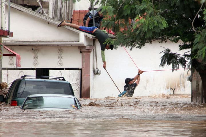 Rescate. Personas ayudan a un miembro de Protección Civil a cruzar para ayudar a otras personas atrapadas por las inundaciones en Chilpancingo.