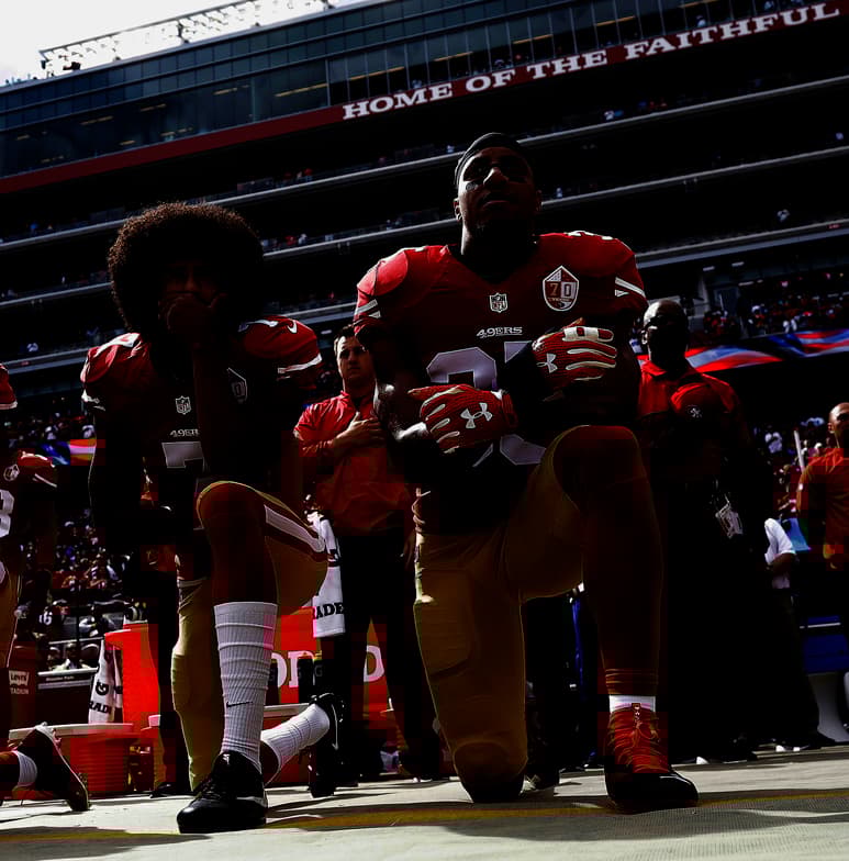 El mariscal de campo Colin Kaepernick (i) y el safety Eric Reid (d) se hincan durante el himno nacional de los Estados Unidos en un partido de 2016. (AGENCIA)
