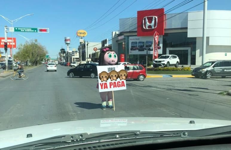 La persona dentro de la botarga, muestra a los automovilistas la pancarta que señala la supuesta deuda de 'Jorge' (CAPTURA)
