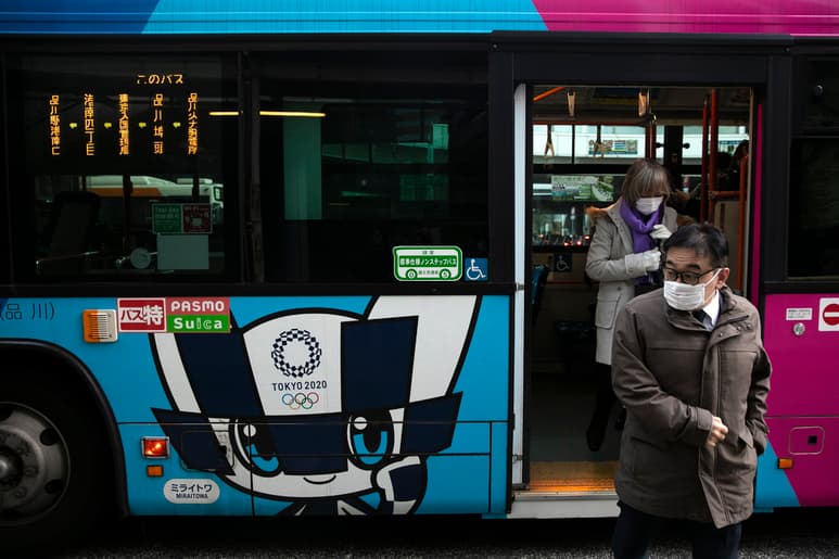 Pasajeros luciendo cubrebocas se bajan de un autobús con publicidad de los Juegos Olímpicos de Tokio 2020. (AP)