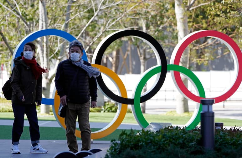 Visitantes con cubrebocas caminan cerca de los Aros Olímpicos en el Estadio Nacional de Tokio. (EFE)