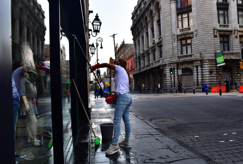 Una trabajadora de un local comercial limpia los vidrios externos del negocio este martes en el Centro Histórico. (EFE)