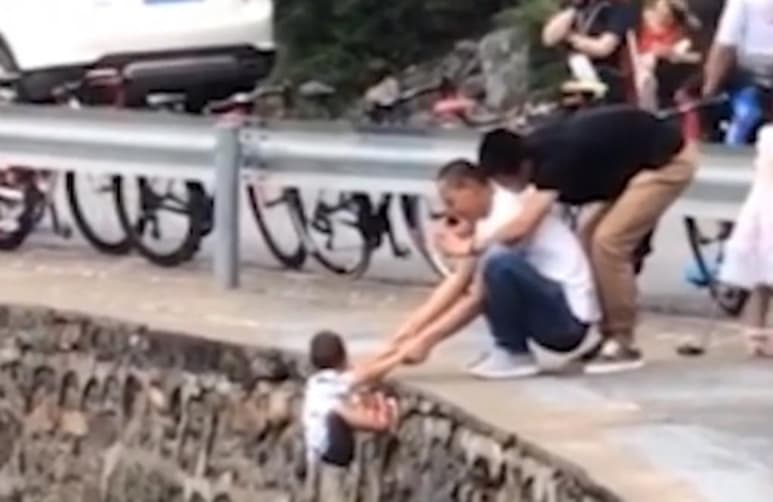 Desde atrás, otro sujeto tomaba la fotografía mientras el niño colgaba del acantilado sostenido de los brazos por quien se piensa es su padre (CAPTURA)