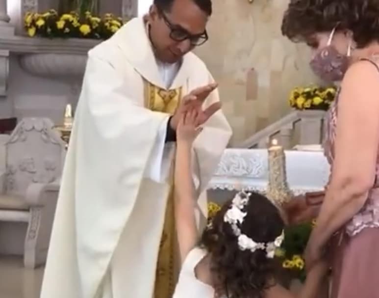 En el video aparece caminando de la mano de su madrina para llegar y recibir la bendición del padre, pero al colocarle la mano sobre la cabeza para realizar la acción, la pequeña confunde la seña y 'las choca' con él. (Especial)