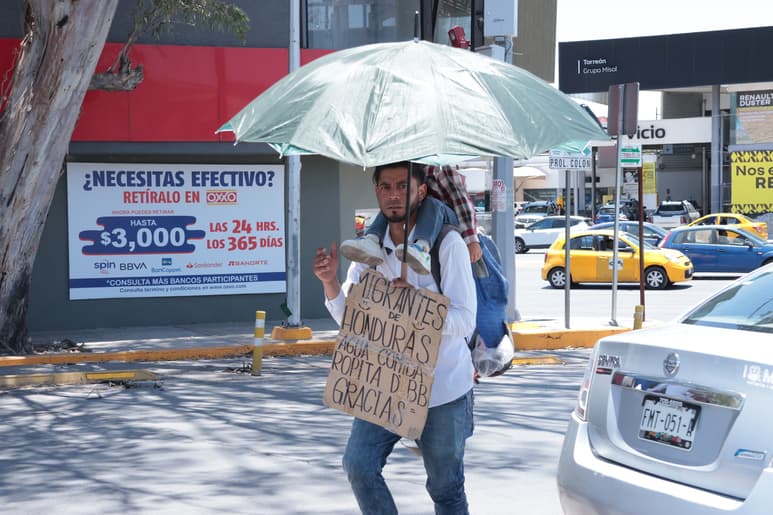 Migrante se protege del sol con una sombrilla en un crucero de Torreón. (VAYRON INFANTE)